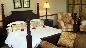 A hotel room with a four-poster bed, a nightstand with a lamp, a striped armchair, and a floral-patterned sofa.