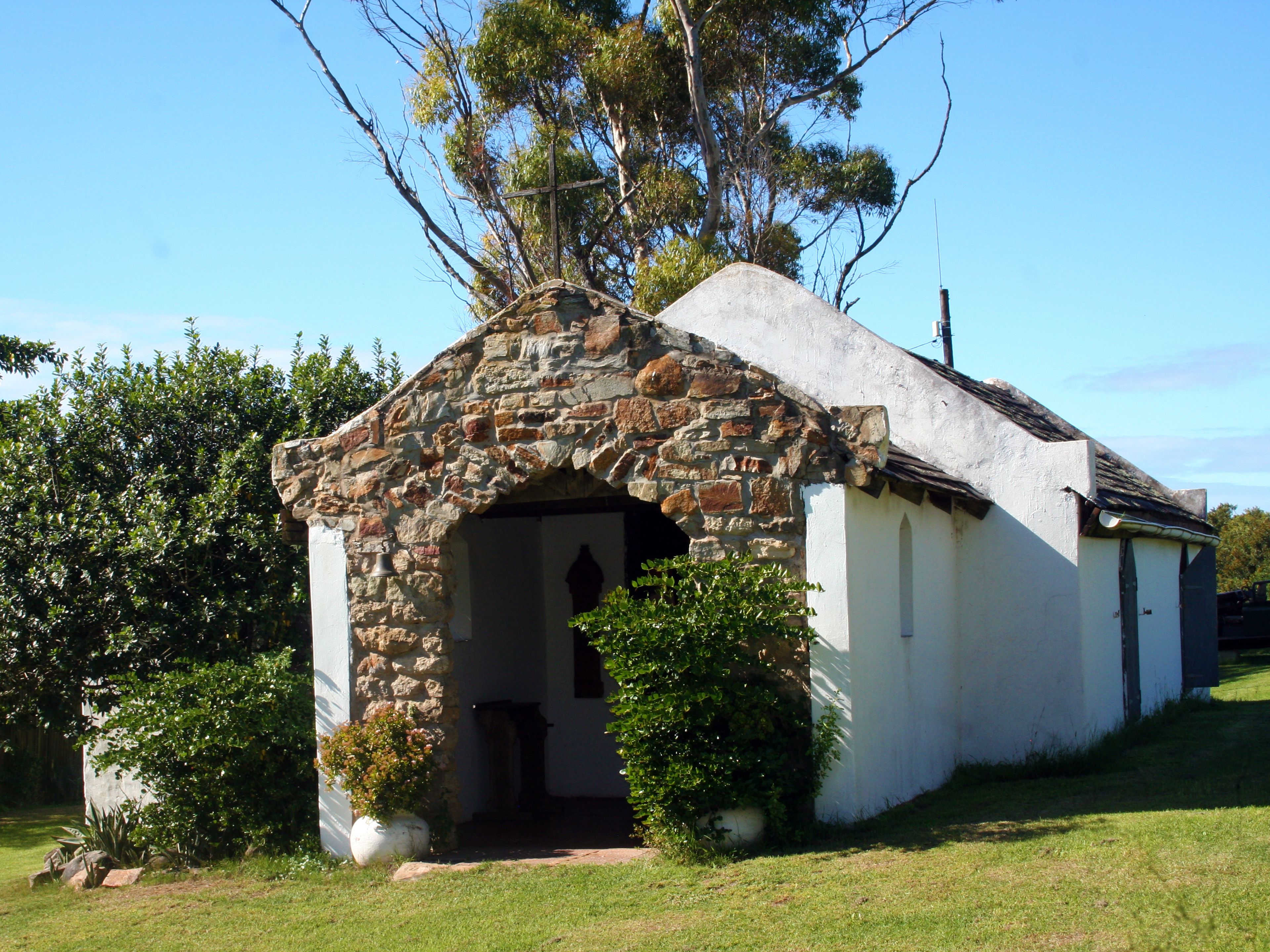 A small stone building with a white exterior, a single entrance, and a bell.