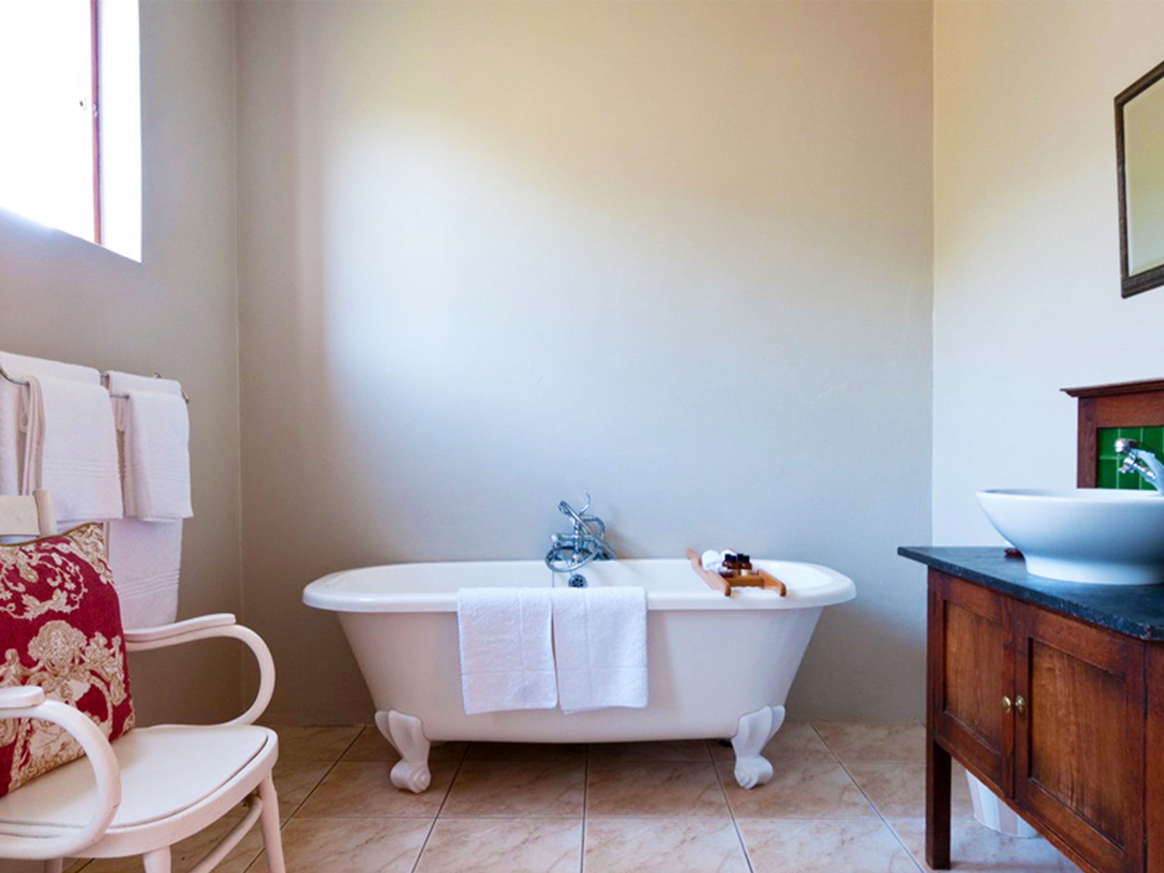 Une salle de bain avec une baignoire sur pieds, une chaise blanche et un meuble-lavabo en bois avec un évier.