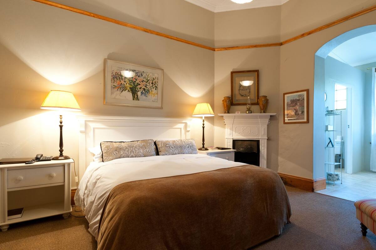 Une chambre à coucher avec un grand lit, deux tables de chevet, une cheminée et un couloir menant à une salle de bain.