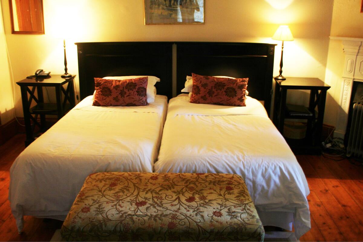 Un lit double avec des oreillers à motifs floraux, une table de chevet avec une lampe et un tableau au mur.
