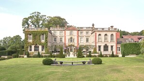 Un grand bâtiment historique à la façade symétrique, doté de nombreuses fenêtres et bordé d’une pelouse bien entretenue, au centre de laquelle se trouve une fontaine.