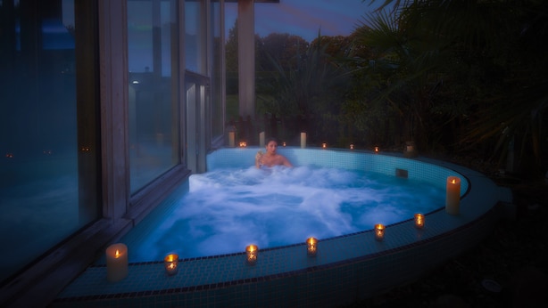 Un bain à remous avec des bougies, entouré de murs de verre et de plantes.