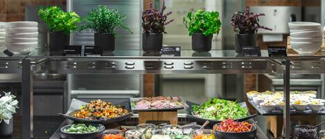 A buffet with various food items and potted plants.