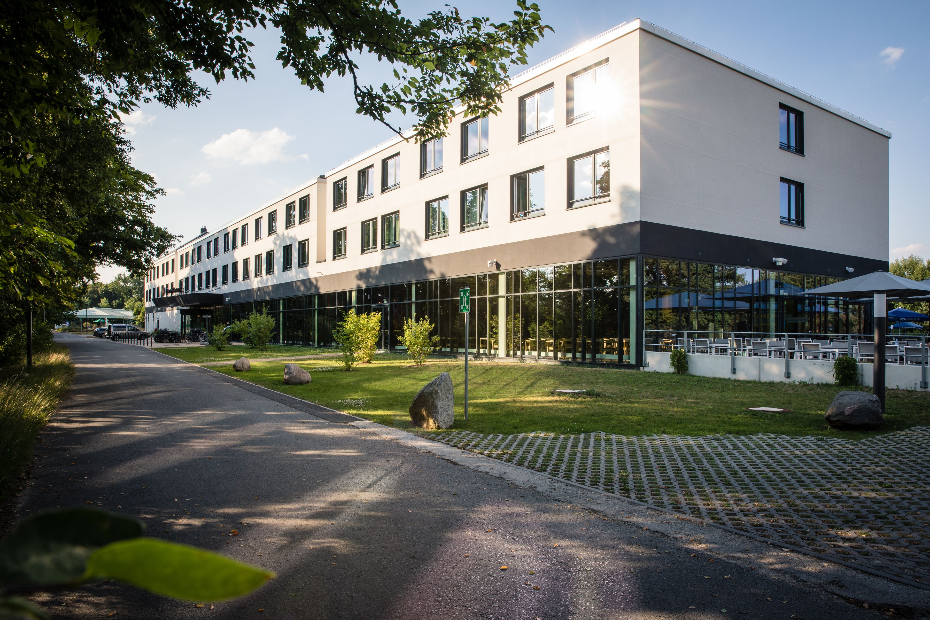 Un bâtiment moderne doté d’un toit plat, de grandes fenêtres et d’un espace pavé aménagé avec des sièges extérieurs.