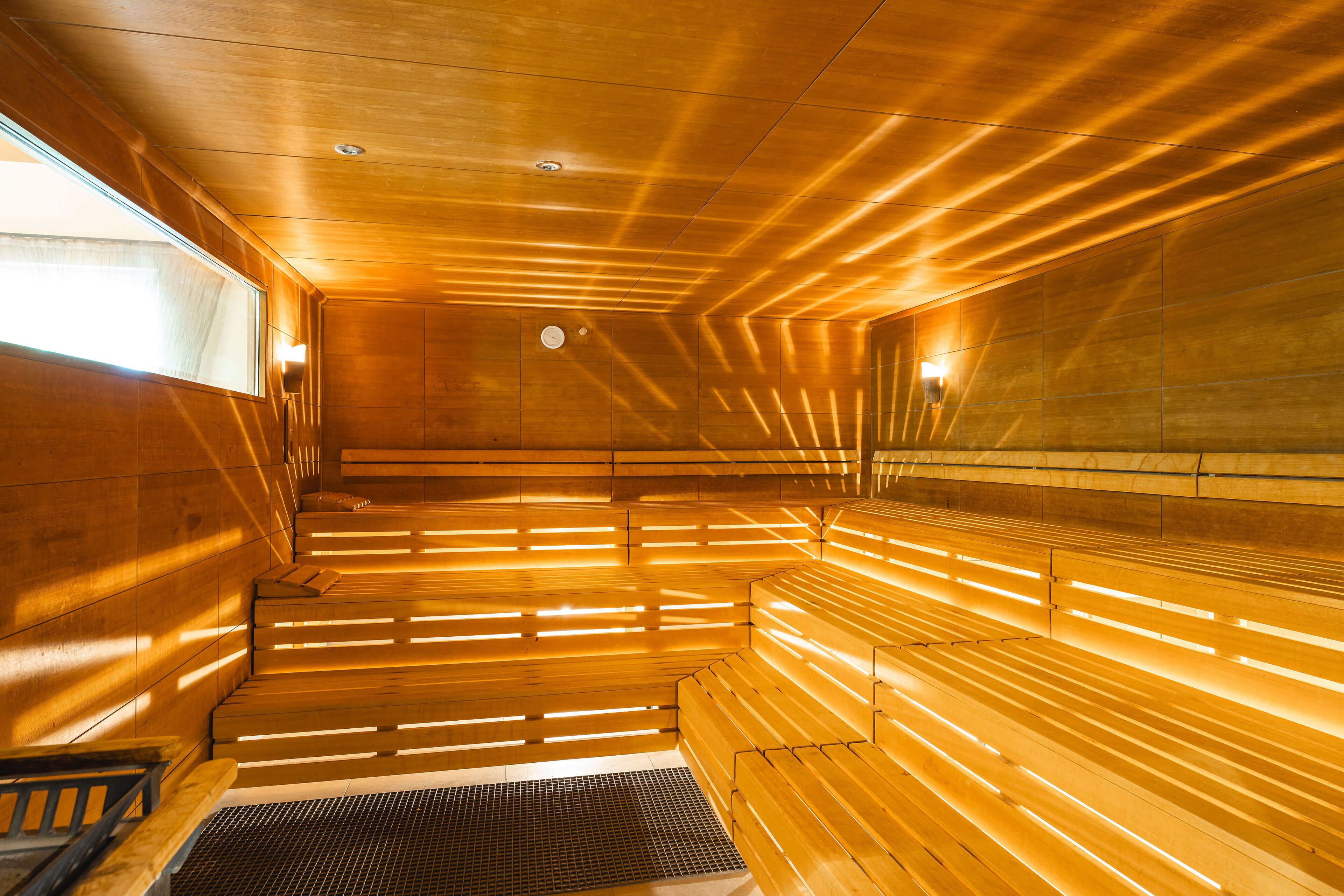 A sauna with wooden benches and slatted walls, illuminated by warm lighting.