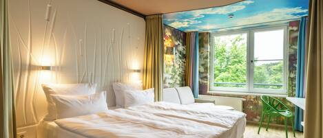 Una habitación de hotel con una cama, una silla, un escritorio y una ventana que ofrece vistas a zonas verdes.
