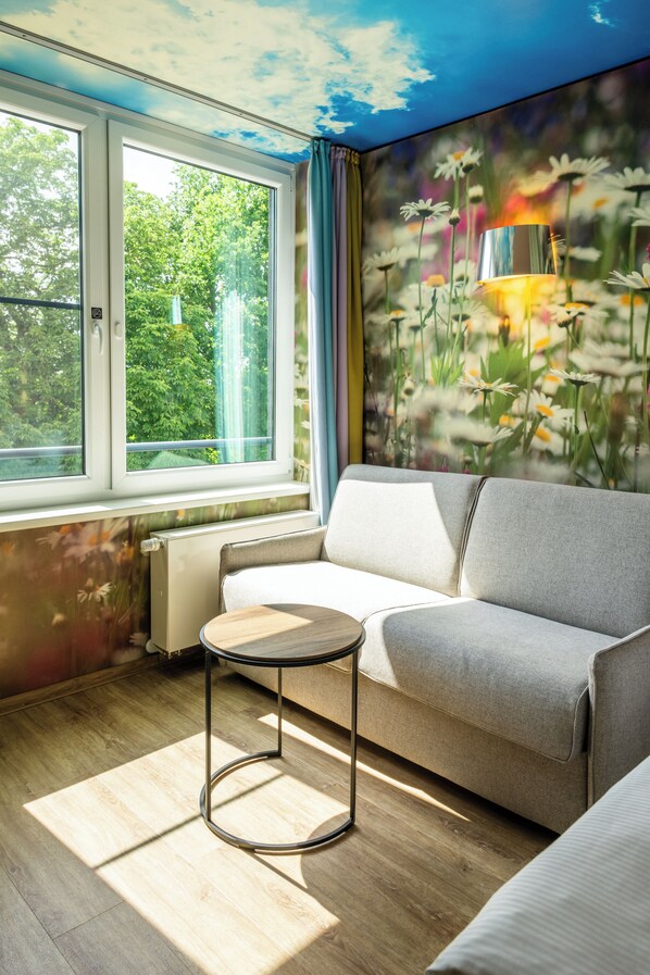 A room with a sofa, a small round table, a radiator, and a window with a view of greenery. - aja Bad Saarow (Bad Saarow)