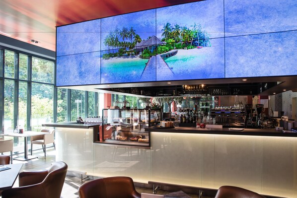 A modern bar area with a large screen displaying a tropical scene, a well-lit bar counter, and seating arrangements. - aja Bad Saarow (Bad Saarow)