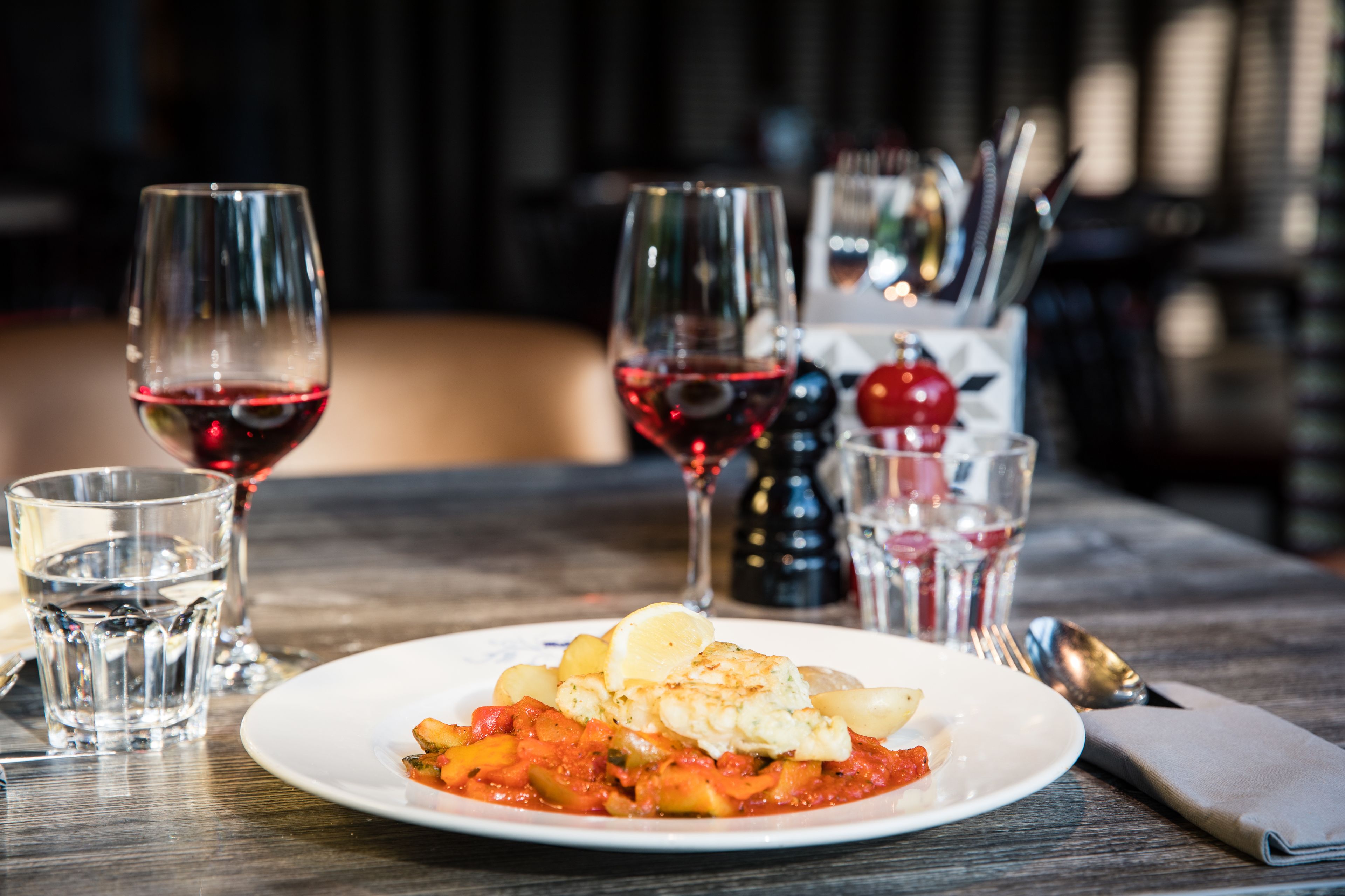 Une table à manger avec une assiette de nourriture, des verres de vin rouge et un salier et un poivrier.