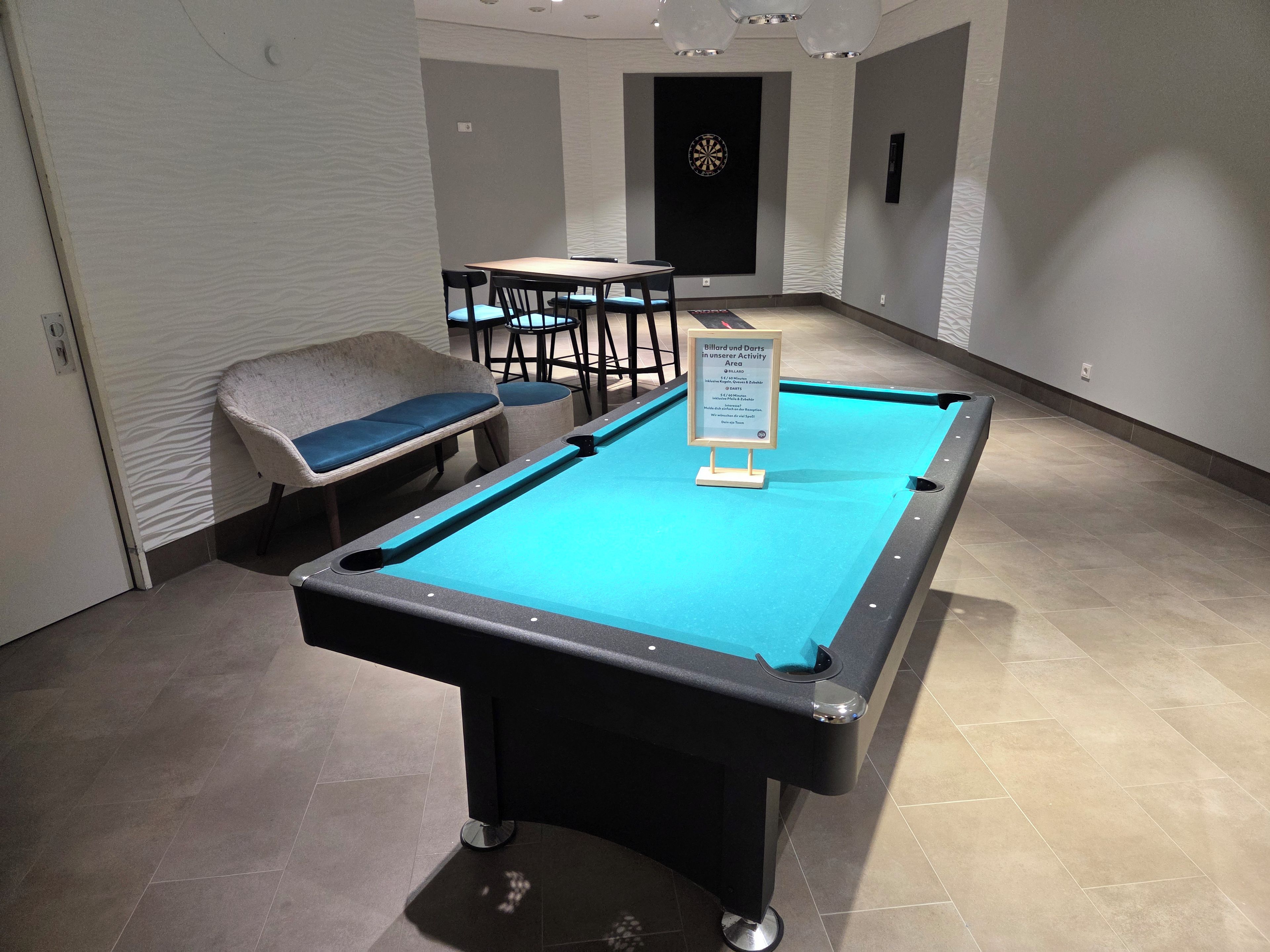 Ein Billardtisch mit Schilder, Stühle und einer Dartscheibe in einem Raum mit Fliesenboden.