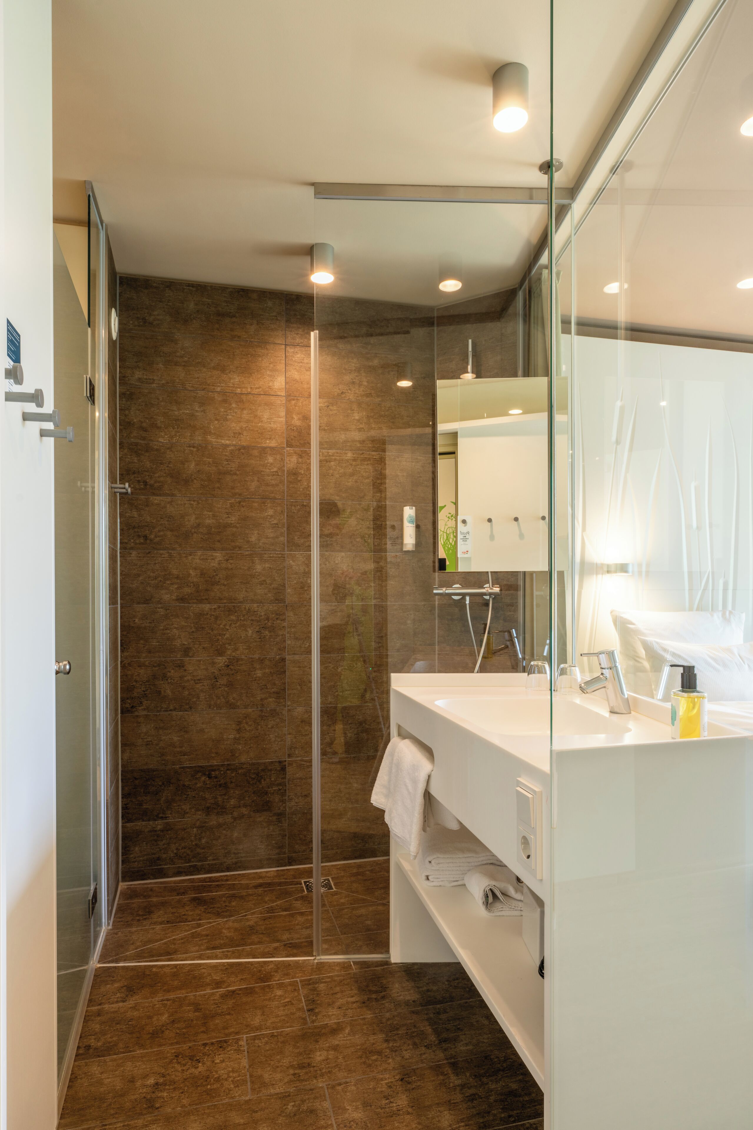 Un baño moderno con cabina de ducha de vidrio, tocador blanco con espejo y lavamanos.