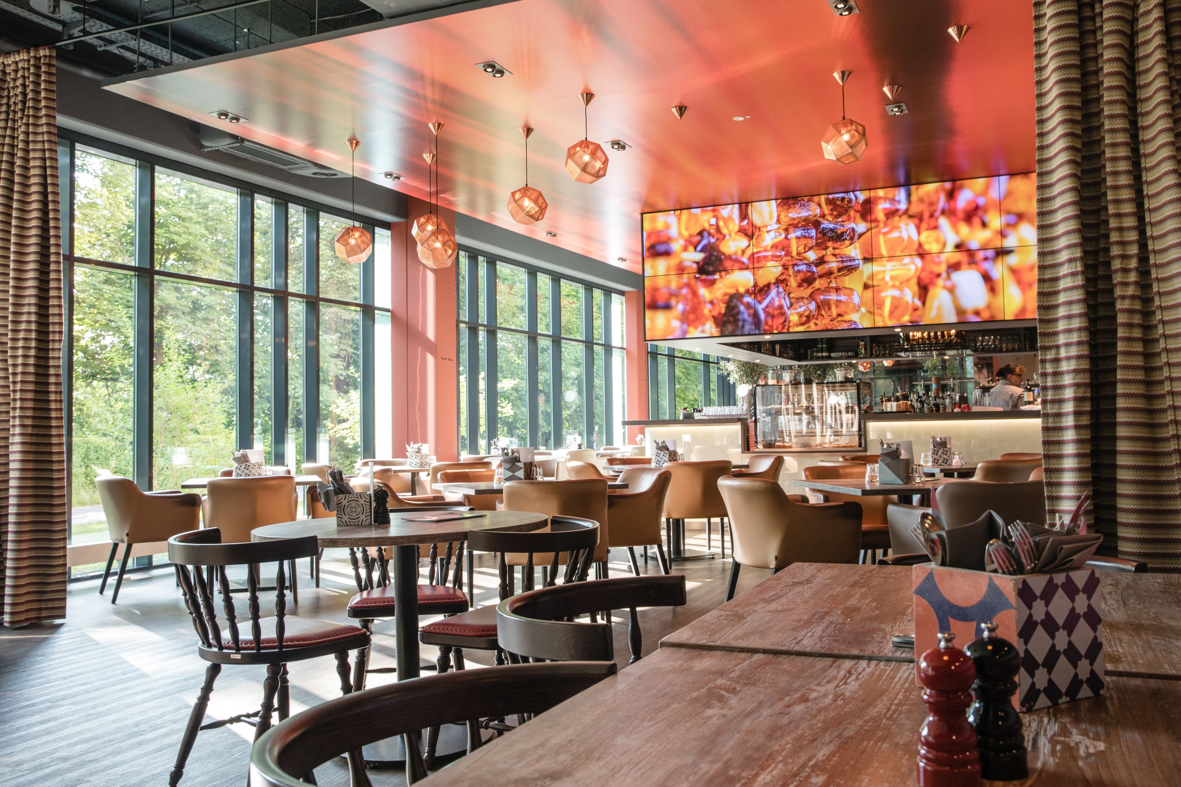 Un restaurant doté de grandes fenêtres, de nombreuses tables et de luminaires suspendus.