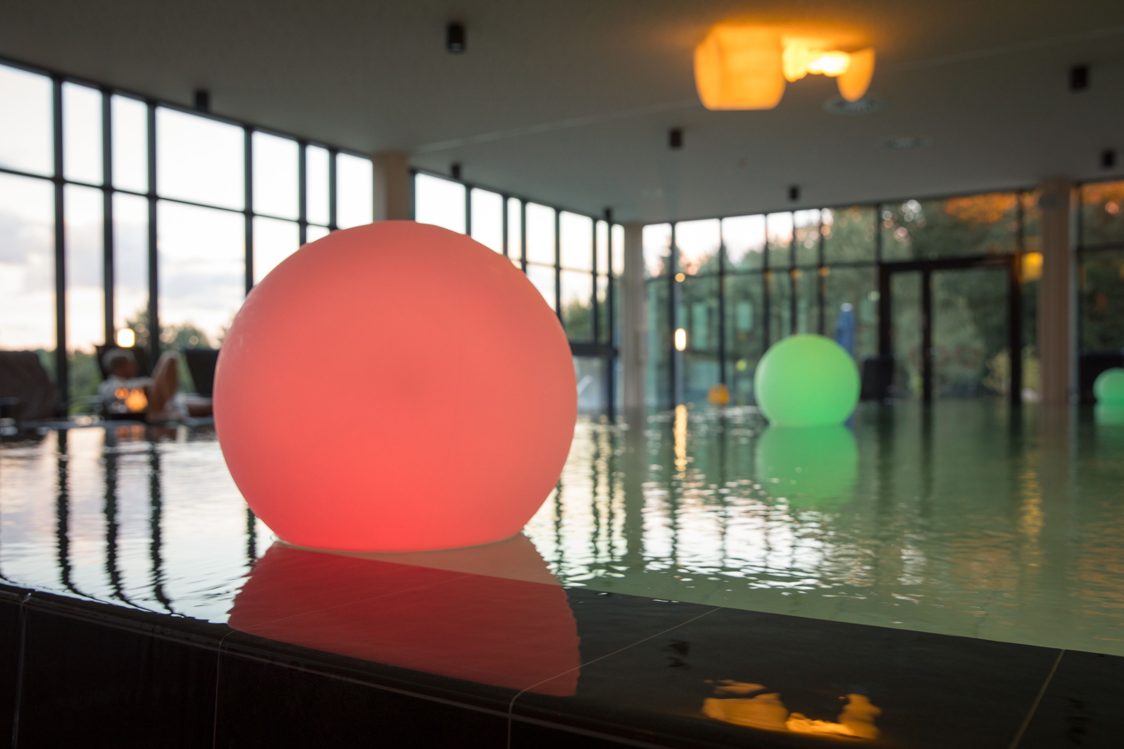 Un área de piscina interior moderna con grandes esferas iluminadas y vistas al exterior a través de amplios ventanales.