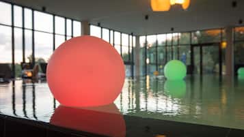 Un área de piscina interior moderna con grandes esferas iluminadas y vistas al exterior a través de amplios ventanales.