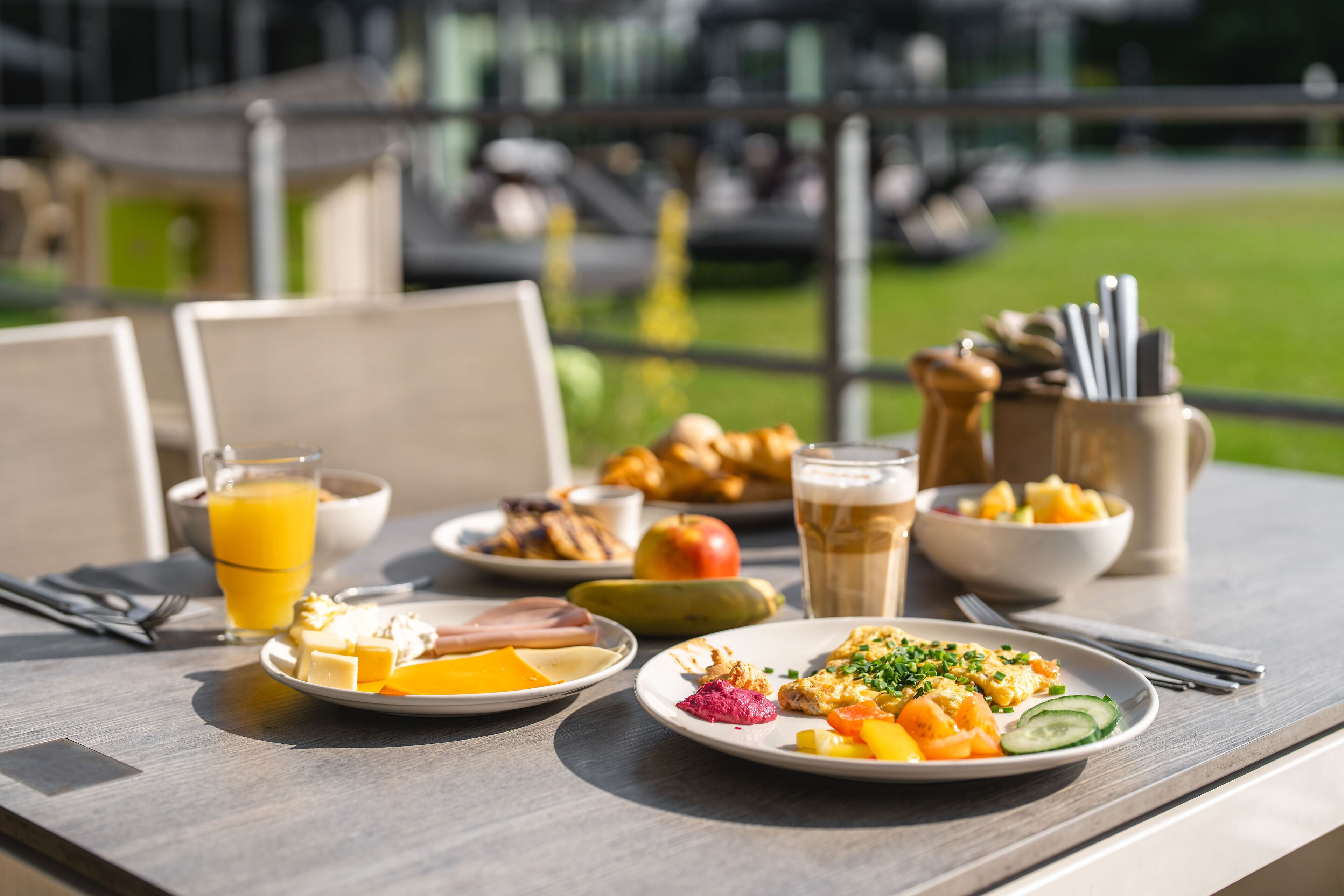 A breakfast table with plates of food, a glass of orange juice, and a beer mug.