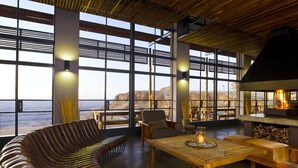 A modern interior with large windows, a wooden ceiling, and a seating area with a table and chairs. - Fish River Lodge (Fish River Canyon)