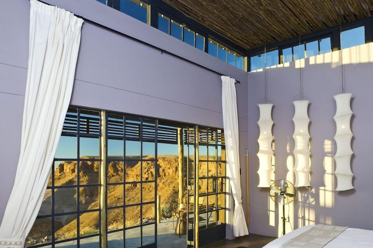 A bedroom with a large window, a bed, and a view of a mountainous landscape.
