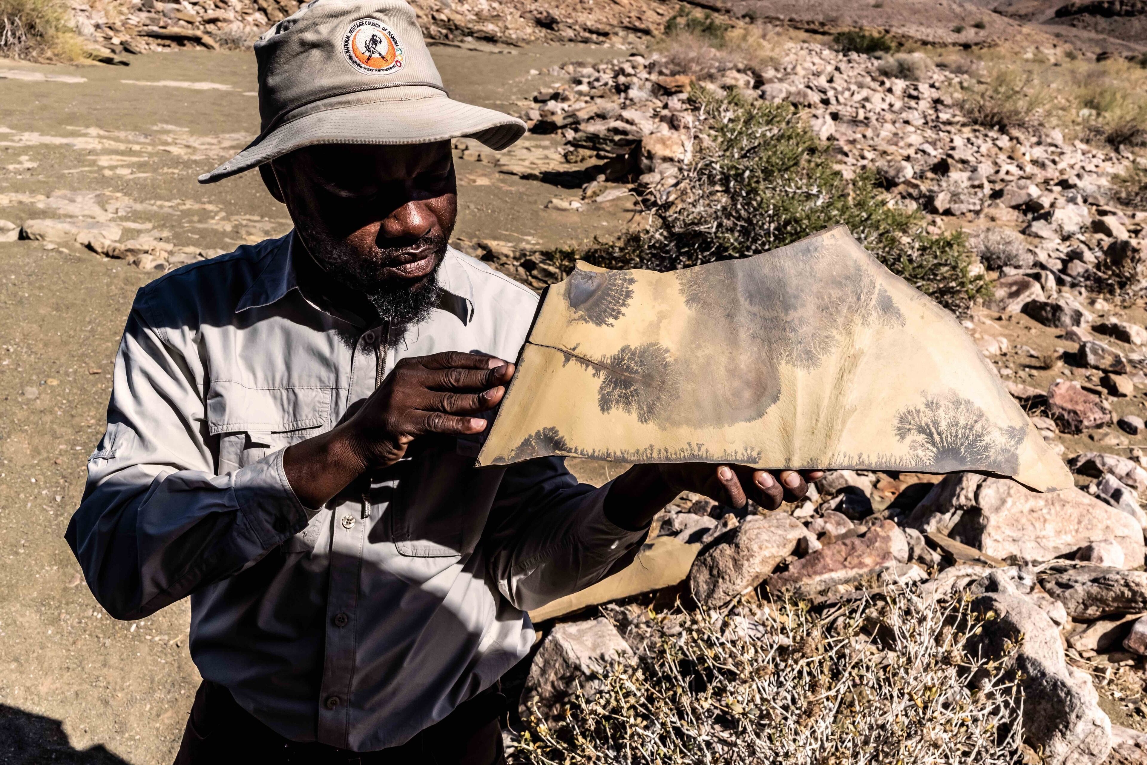 A person holding a map outdoors with a rocky terrain in the background.