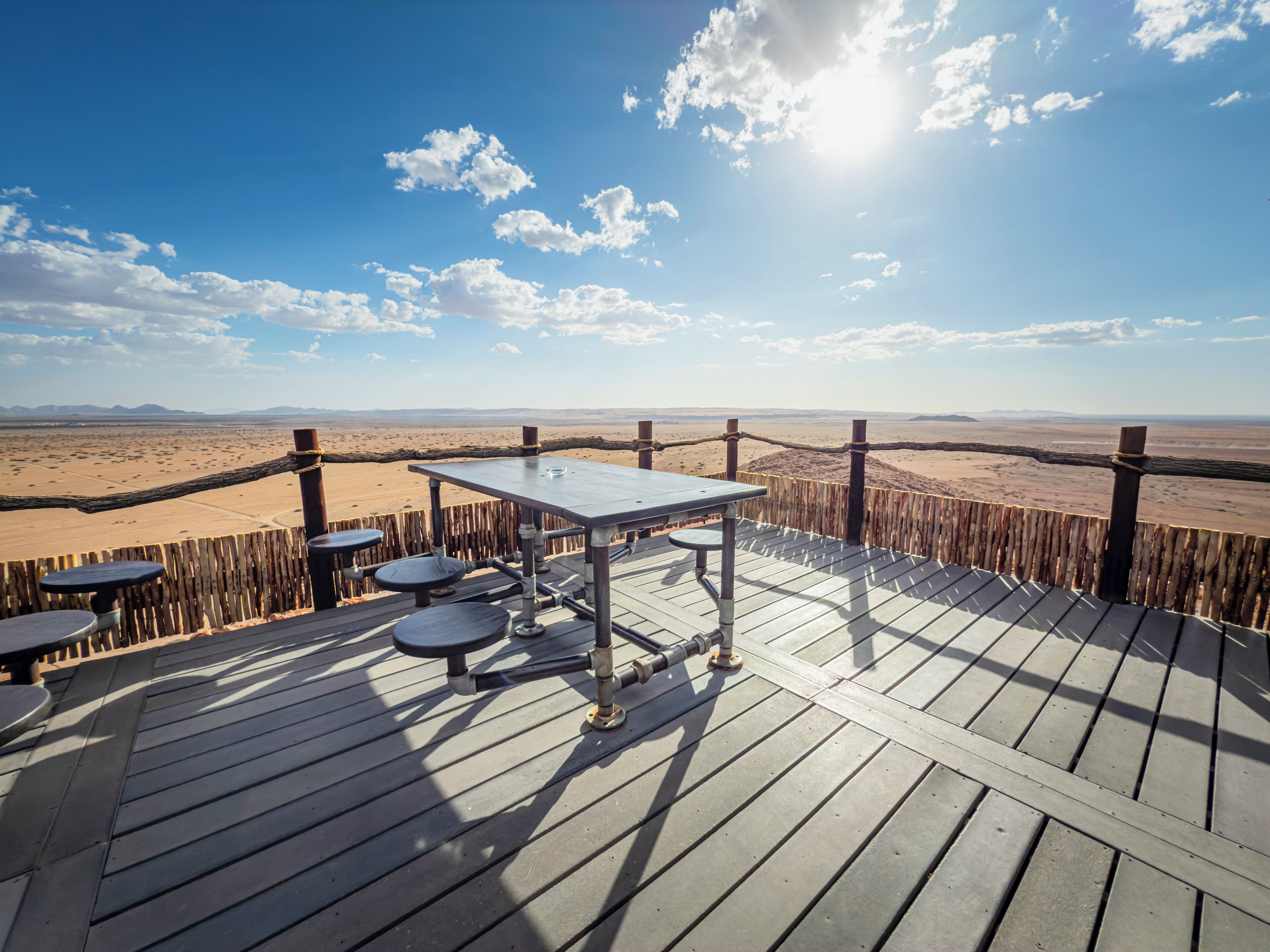 Una terraza de madera con mesas y sillas que da a un paisaje desértico.