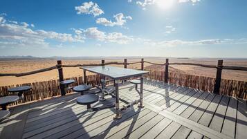 A wooden deck with tables and chairs overlooking a desert landscape.