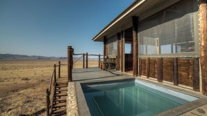 A pool area with a wooden deck and stone border, surrounded by a desert landscape. - Moon Mountain Lodge (Solitaire)
