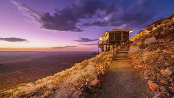 A stone staircase leading to a wooden structure with a balcony, overlooking a vast landscape at dusk.