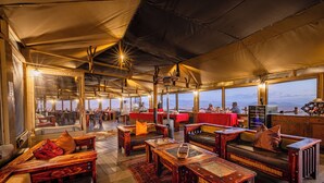 A spacious tented area with wooden furniture, tables, and benches, featuring large windows offering views of the landscape. - Moon Mountain Lodge (Solitaire)