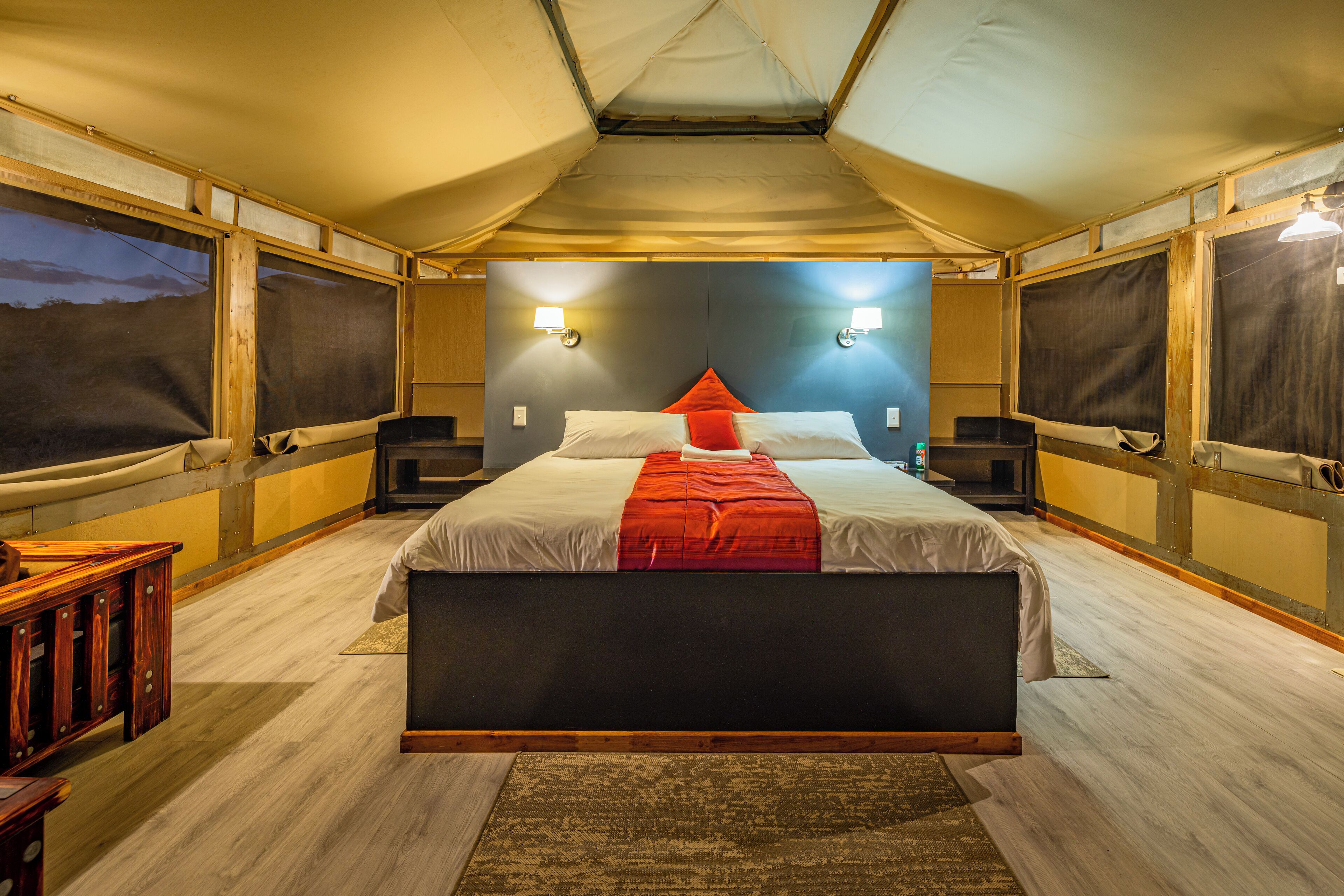 A tent-style room with a bed, two nightstands, and a wooden bench.