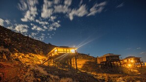A rustic wooden cabin with a balcony, situated on a hillside under a starry night sky. - Moon Mountain Lodge (Solitaire)