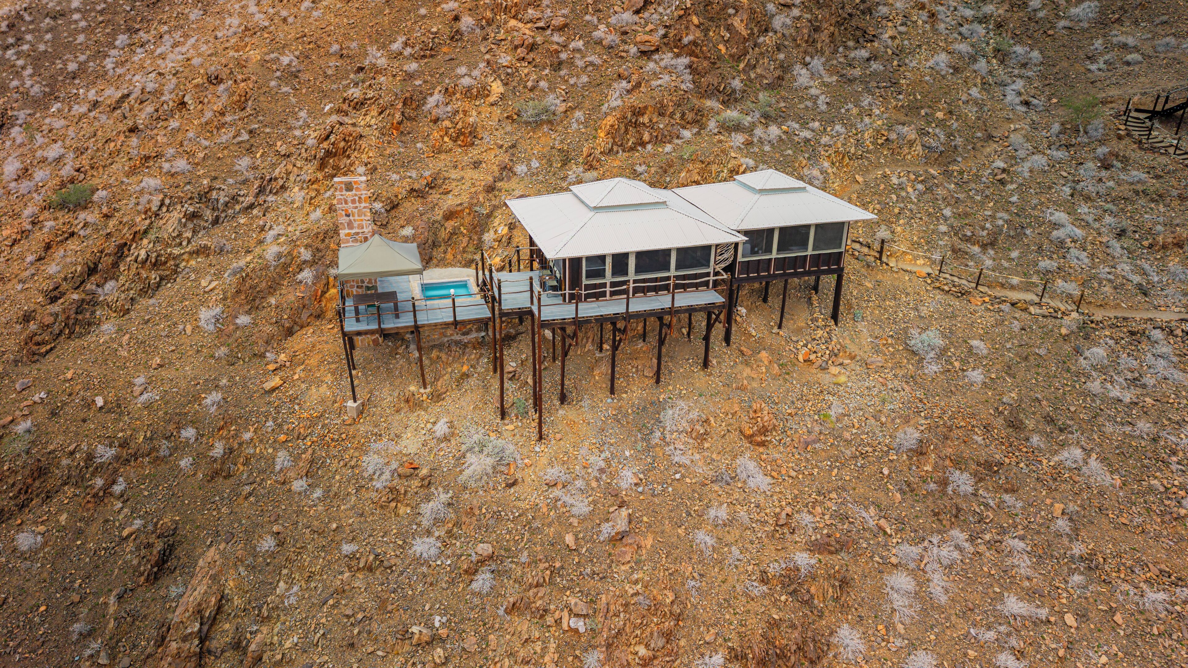 A remote, elevated cabin with a swimming pool, surrounded by rocky terrain and sparse vegetation.