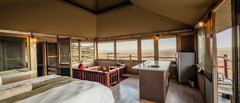 A spacious room with a large bed, a small kitchenette, and a seating area with a view of the desert.