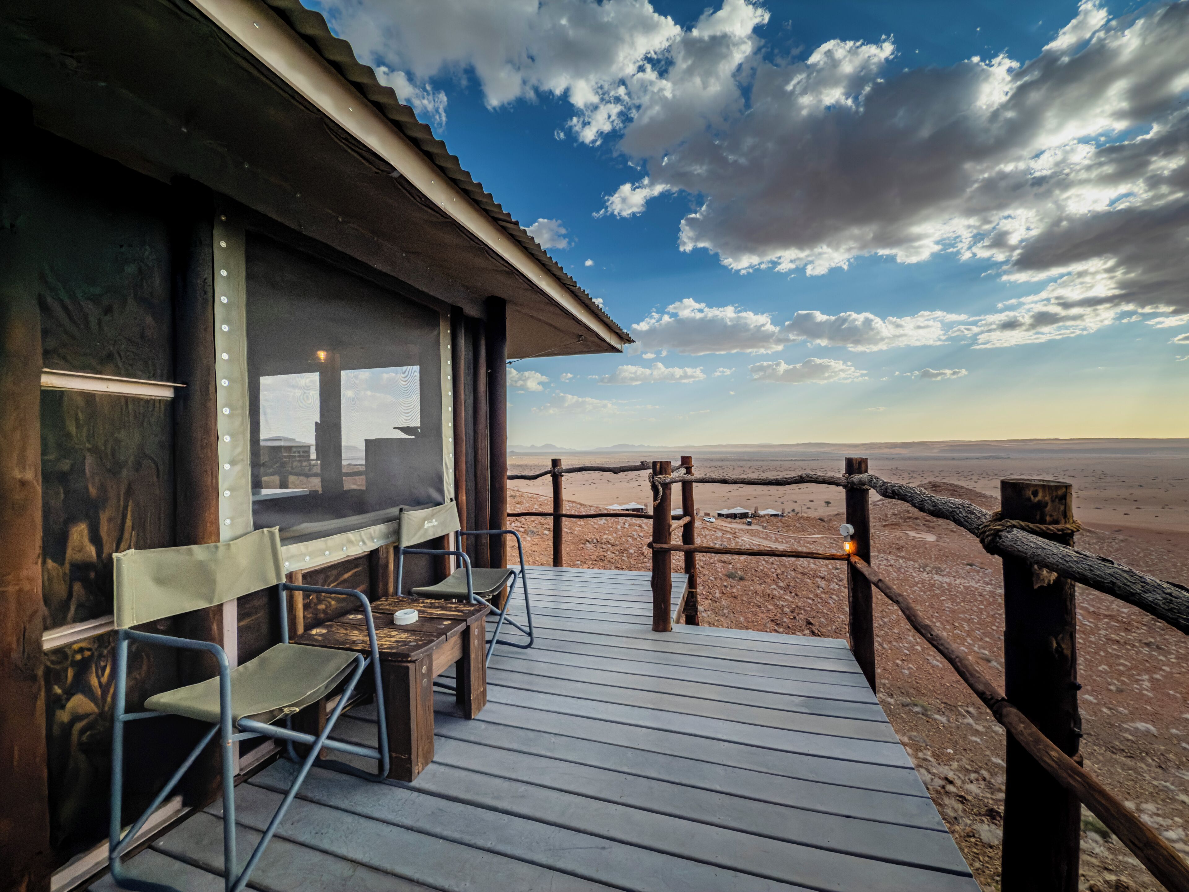 Une terrasse en bois, avec des chaises et une table, d’où l’on peut admirer un paysage désertique.