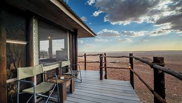 A wooden deck with chairs and a table, overlooking a desert landscape.