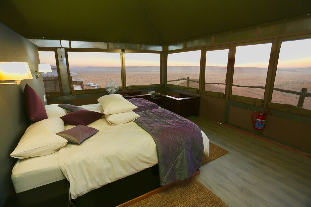 A bedroom with a bed, pillows, a desk, and a view of the desert.