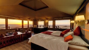 A bedroom with a large bed, a desk, and a view of the sunset over the ocean. - Moon Mountain Lodge (Solitaire)