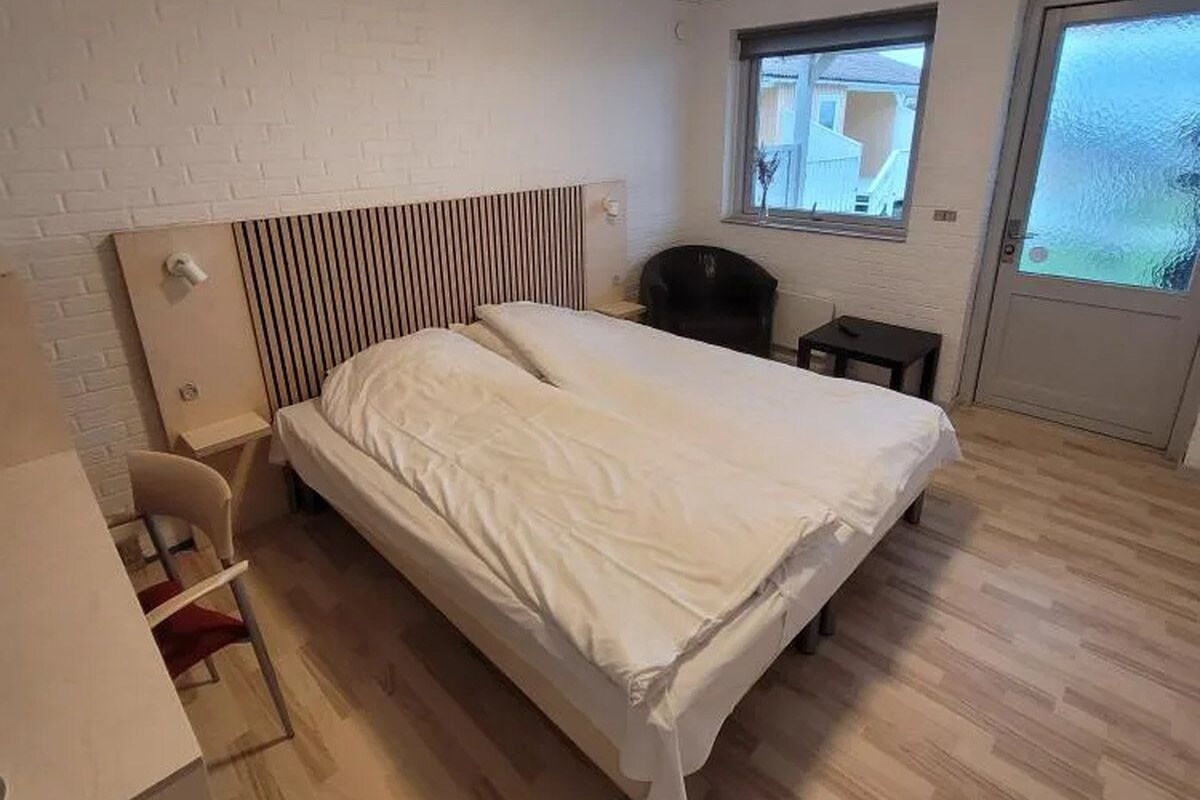 A bedroom with a bed, a desk, a chair, a radiator, a window, and a door.