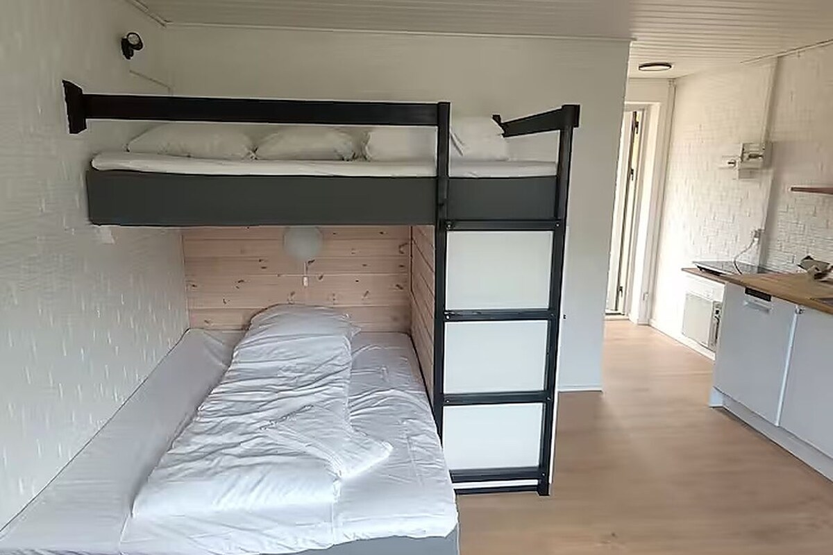 A bunk bed with a desk and a chair in a room with wooden flooring and white walls.
