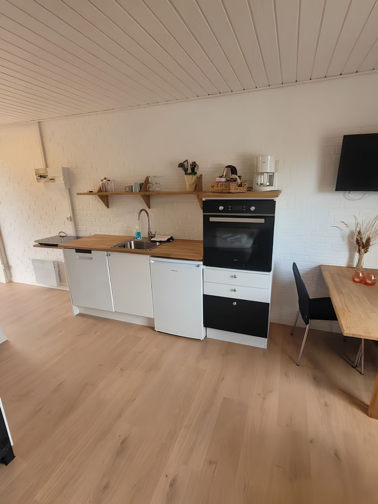 A compact kitchen with a built-in oven, a coffee maker, and a dining area with a table and chairs.