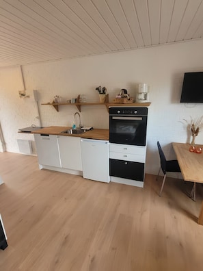 Cocina compacta con horno integrado, cafetera y comedor con mesa y sillas.