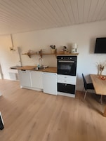 A compact kitchen with a built-in oven, a coffee maker, and a dining area with a table and chairs.