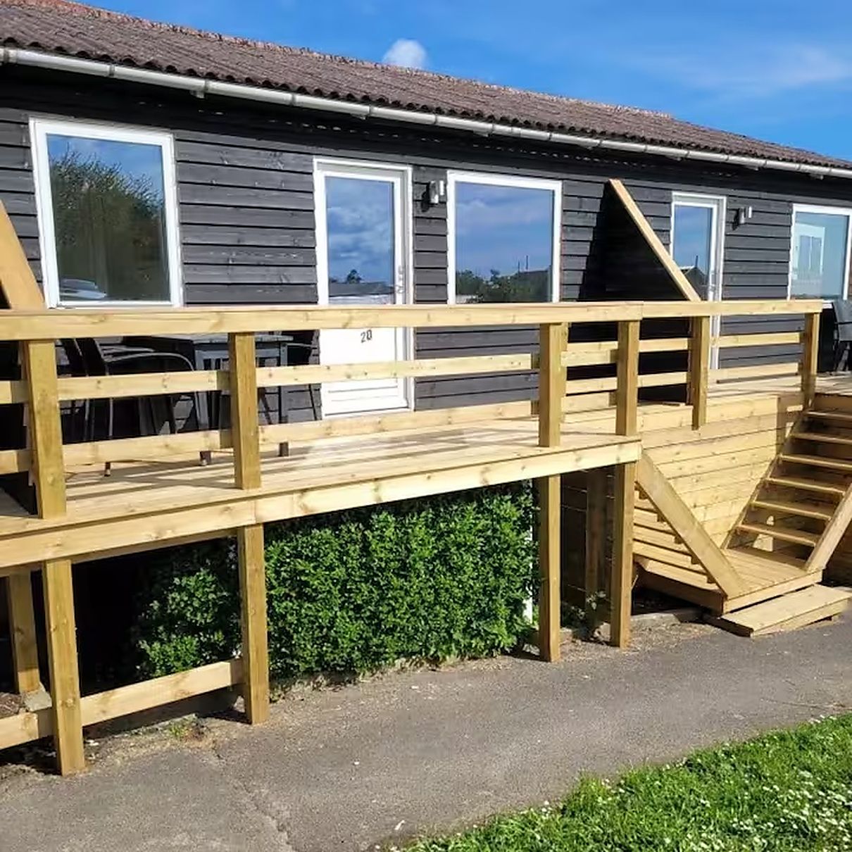 Una terraza de madera con una rampa que lleva a un edificio con varias ventanas.
