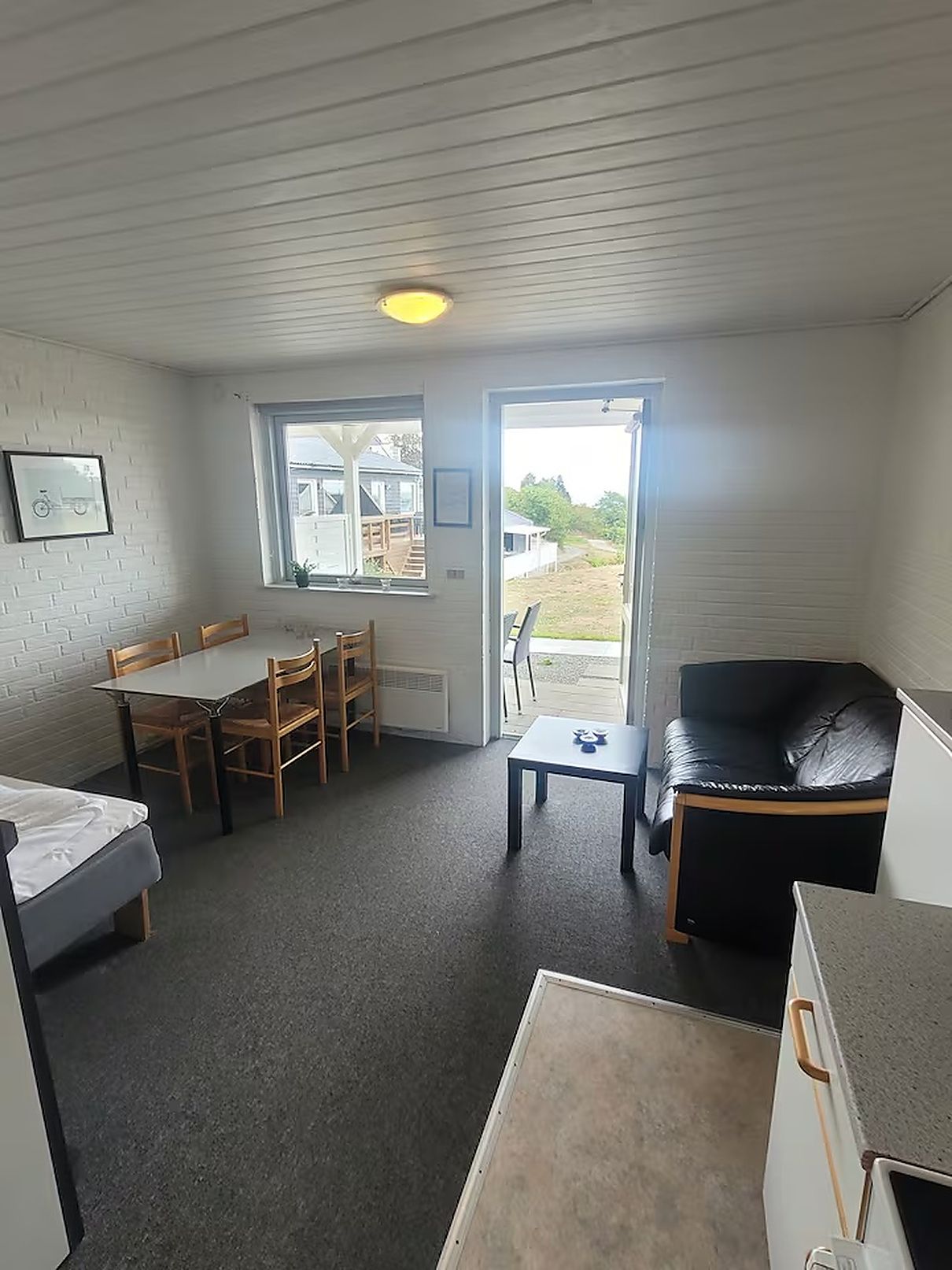 A compact room with a dining table, chairs, a black leather sofa, a small table, and a bed.