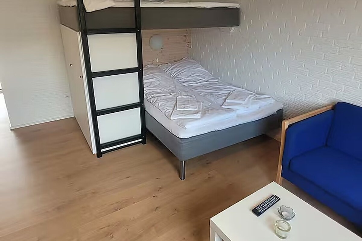 A bunk bed with a ladder, a single bed, a blue sofa, and a small white table with a remote control and a glass.