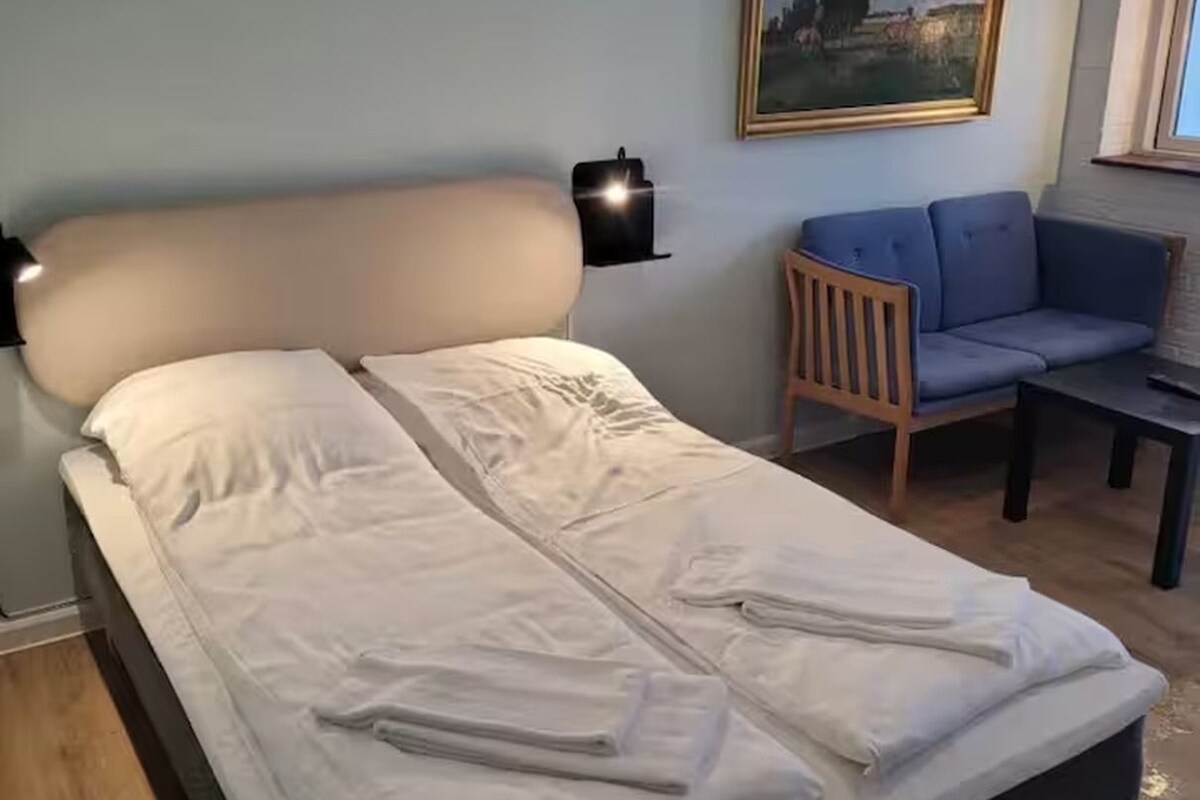 A bed with white linens, a headboard, and a nightstand with a lamp.