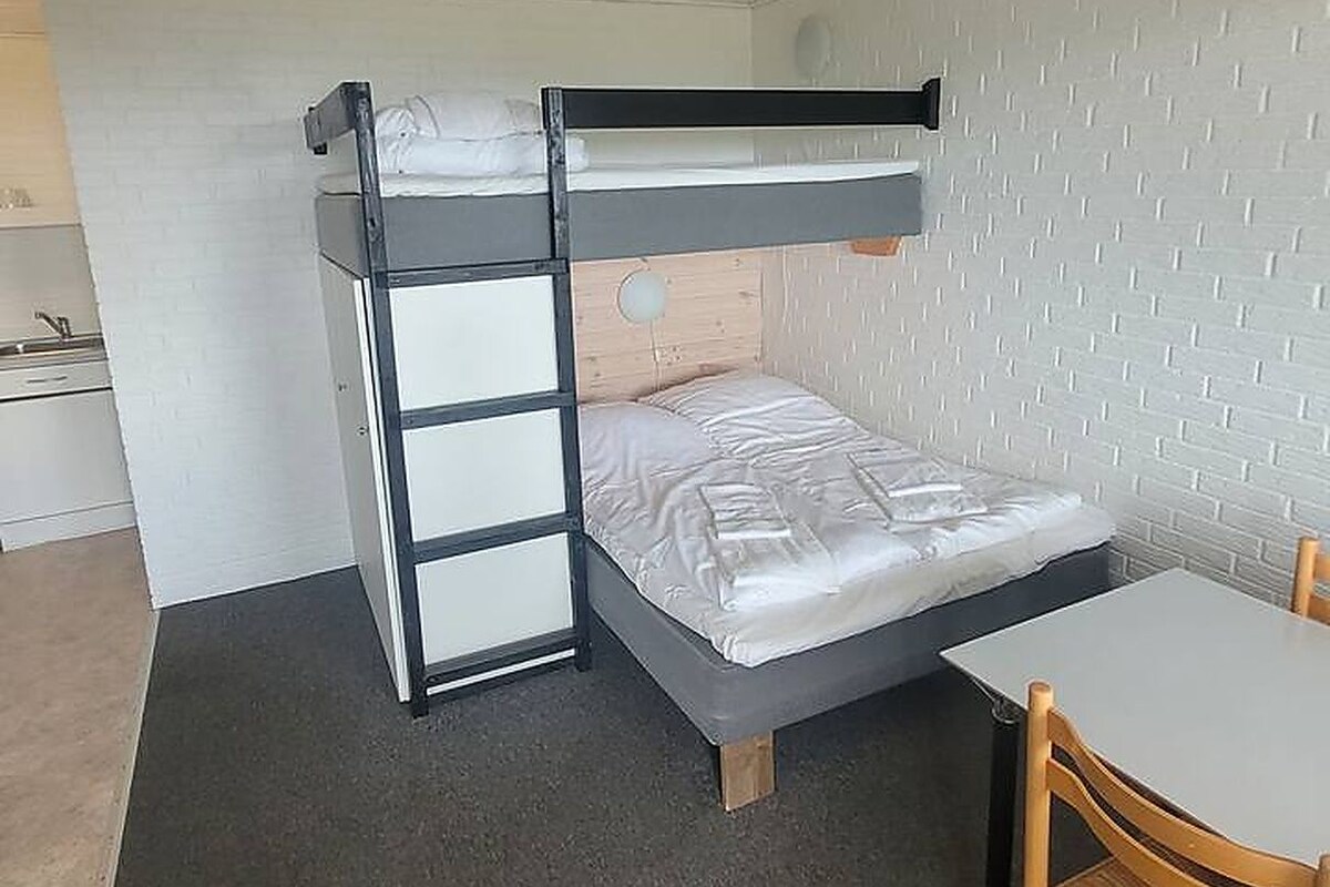A bunk bed with a desk and chair, a small table, and a white brick wall.