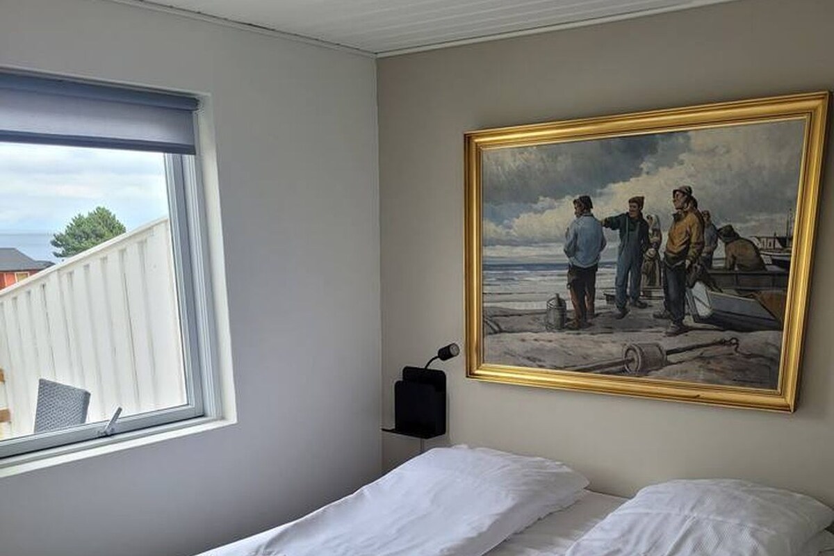 A bedroom with a bed, a window, a painting, and a bedside table.