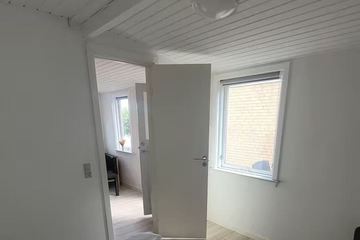 A bedroom with a bed, a window, and a door leading to another room.
