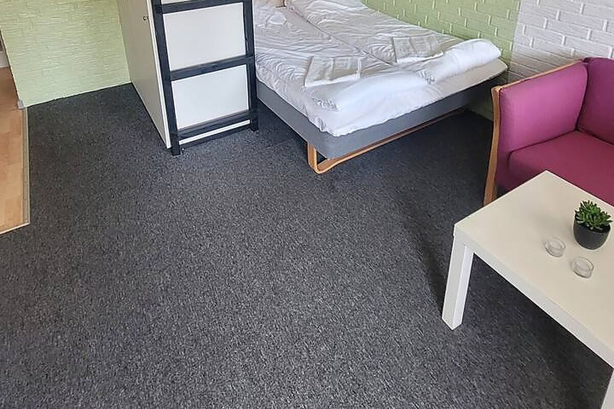A bunk bed with a ladder, a single bed, a small table with a plant, and a pink chair in a room with green and white walls.