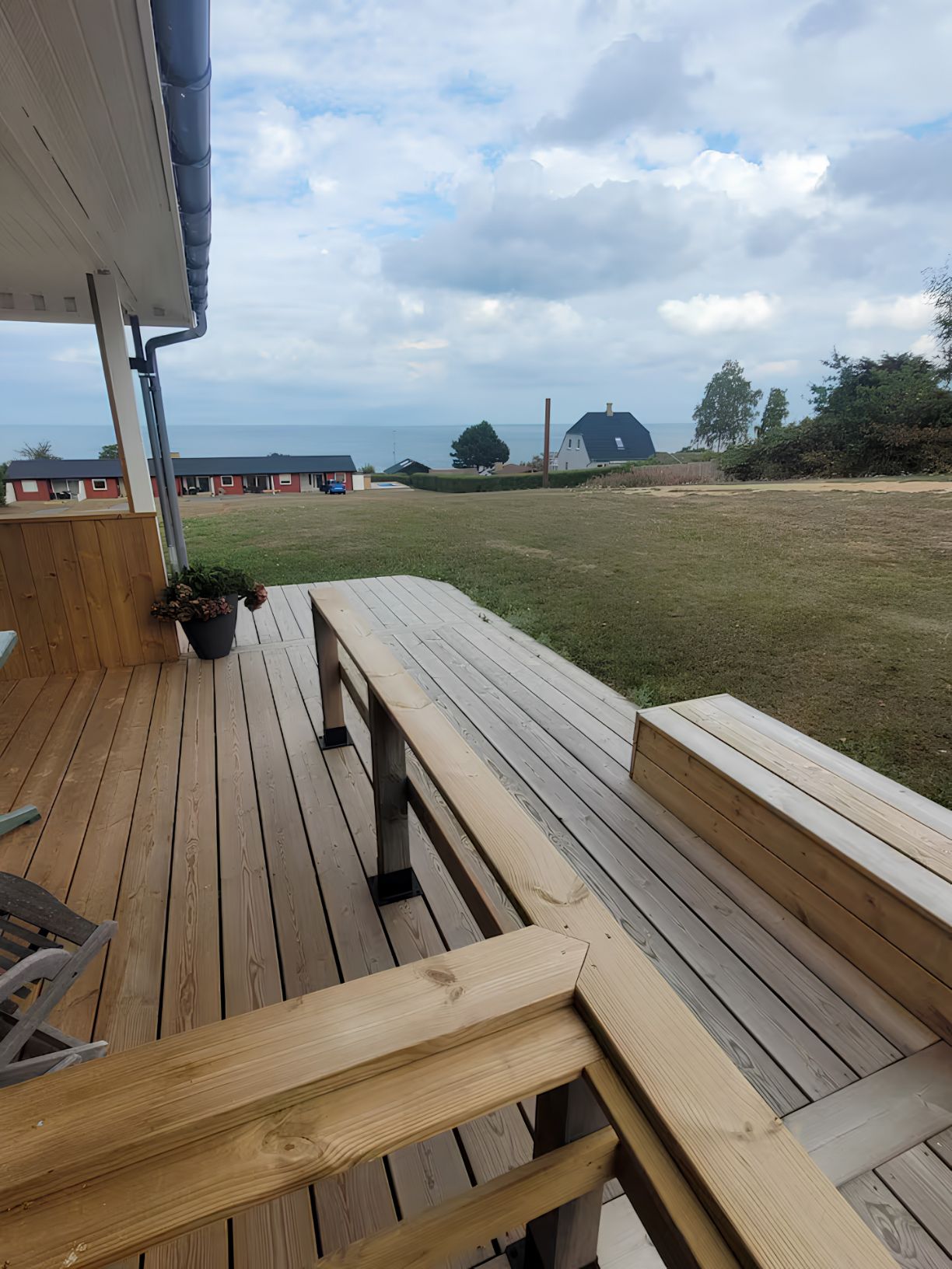A wooden deck with benches overlooking a grassy area and a view of the sea.